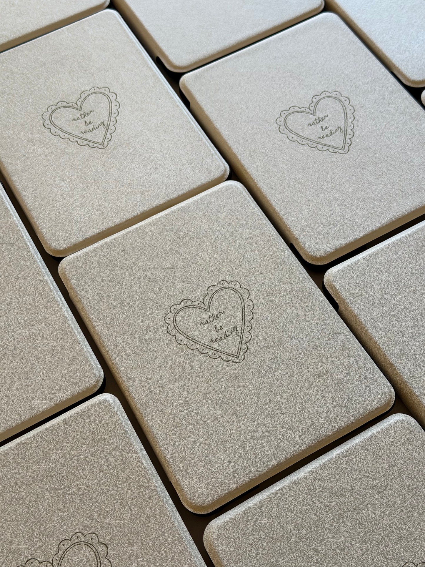 Pearly white case with heart-shaped designs on a textured surface 'rather be reading'